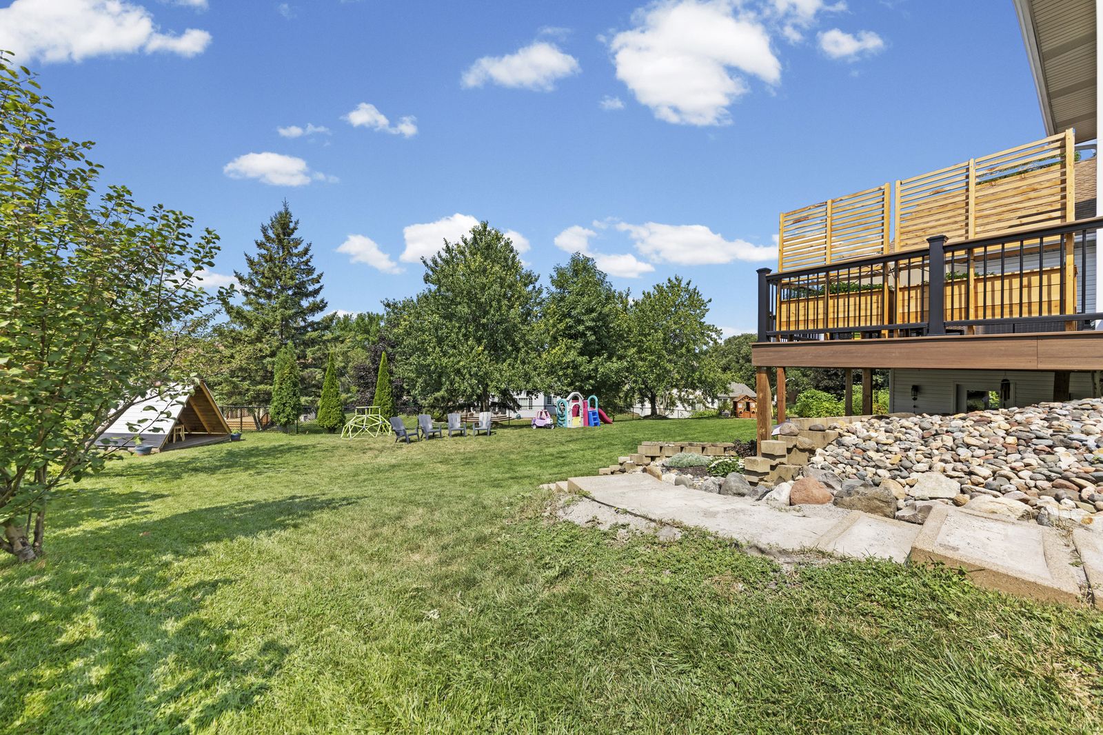 Backyard with lawn, play structures, and deck above
